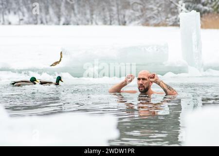 Gutaussehender Junge oder Mann, der im eiskalten Wasser eines gefrorenen Sees zwischen Enten schwimmt. Wim Hof Methode, Kältetherapie, Atemtechniken Stockfoto