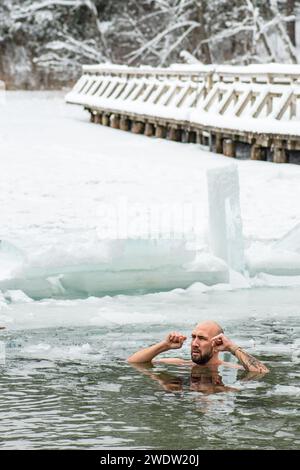 Gutaussehender Junge oder Mann, der im eiskalten Wasser eines gefrorenen Sees zwischen Enten schwimmt. Wim Hof Methode, Kältetherapie, Atemtechniken, vertikal Stockfoto