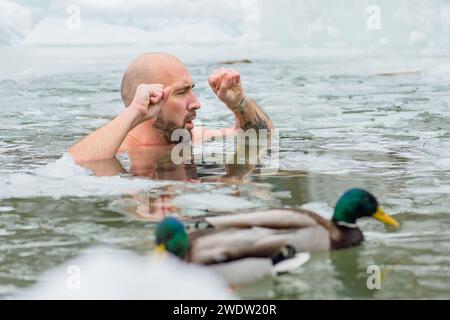 Gutaussehender Junge oder Mann, der im eiskalten Wasser eines gefrorenen Sees zwischen Enten schwimmt. Wim Hof Methode, Kältetherapie, Atemtechniken Stockfoto