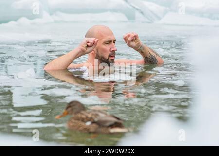 Gutaussehender Junge oder Mann, der im eiskalten Wasser eines gefrorenen Sees zwischen Enten schwimmt. Wim Hof Methode, Kältetherapie, Atemtechniken Stockfoto