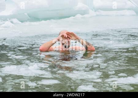 Gutaussehender Junge oder Mann, der im eiskalten Wasser eines gefrorenen Sees zwischen Enten schwimmt. Wim Hof Methode, Kältetherapie, Atemtechniken Stockfoto