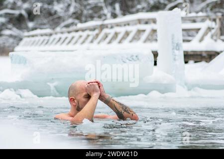 Gutaussehender Junge oder Mann, der im eiskalten Wasser eines gefrorenen Sees zwischen Enten schwimmt. Wim Hof Methode, Kältetherapie, Atemtechniken Stockfoto