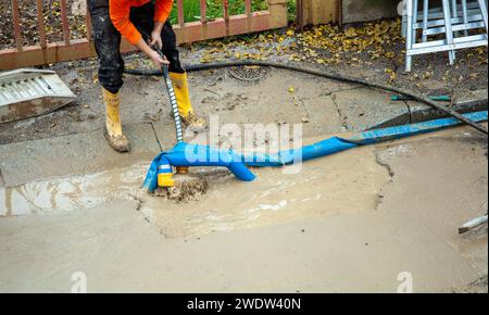 Ein Arbeiter repariert eine kaputte Wasserleitung auf der Straße, indem er eine Pumpe benutzt, um den Graben zu leeren. Stockfoto