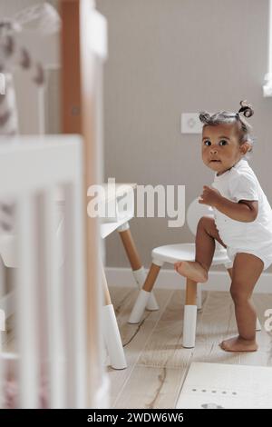 Gemischtes Mädchen, das im Kinderzimmer neben Kindermöbeln spielt. Afrokaukasisches kleines Mädchen. Das Konzept der interrassischen Familie. Stockfoto