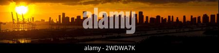 Panorama Sonnenuntergang Silhouette der Innenstadt von Miami von South Beach mit Wolkenkratzern und Kreuzfahrtterminal vor dem orangen Himmel der untergehenden Sonne Stockfoto
