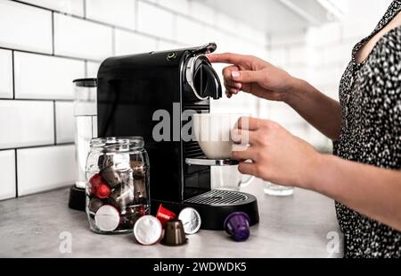 Mädchen mit Kapsel-Kaffeemaschine und Tasse in der Küche. Frau, die italienisches Koffeingetränk mit professioneller Espressomaschine zubereitete Stockfoto