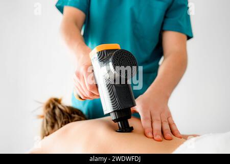 Professioneller Massagetherapeut Rehabilitologe, der Rückenmassage mit einem vibrierenden Massagegerät, Entspannung der Muskelkrämpfe Stockfoto