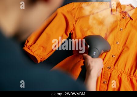 Frau dampfend Kleid mit Handkleidung Dampfgarer auf Sofa zu Hause Stockfoto