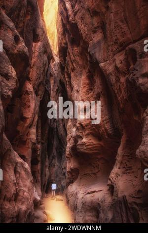 Kleine Person mit weißer Spitze, die in einem tiefen engen Canyon steht. Von hinten. Sonnenlicht Stockfoto