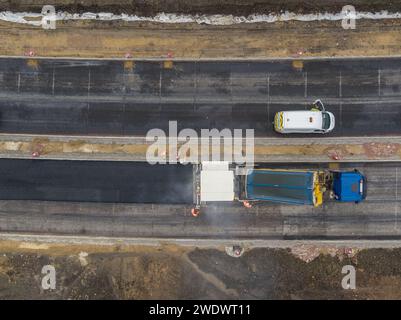 Luftbild mit Blick auf eine Straßenpflastermaschine/Asphaltfertiger, die mit Asphalt von einem Kipper beladen wird, der eine neue Straße verlegt Stockfoto