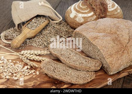 Bio-braune Brotlaibe auf Olivenholzplatte mit Roggenflocken und Korn in einer hessischen Tasche über Eichenhintergrund. Stockfoto