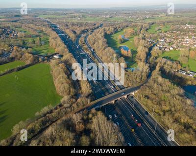 Luftbild der Autobahn M6 in Birchwood, Warrington, Großbritannien, mit Blick nach Norden auf eine Autobahnbrücke und die Abzweigung 21A mit Häusern und Feldern Stockfoto