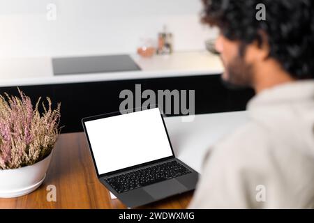 Blick von der Rückseite eines Indianers mit lockigen Haaren auf einem leeren Laptop-Bildschirm, was den wachsenden Trend der Fernarbeit und die Notwendigkeit betont, sich in einem Raum ohne Ablenkung zu konzentrieren. Modell Stockfoto