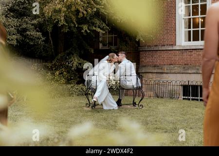 West Sussex, England. Ein junges Paar, das sich an ihrem Hochzeitstag auf einem Liebessitz umschließt und küsst. Stockfoto