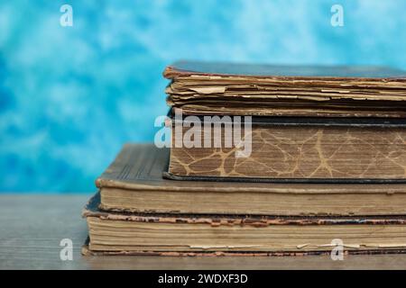 Stapel alter Bücher auf einem Holztisch mit blauem Hintergrund. Stockfoto