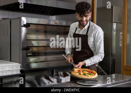 Ein lächelnder Koch bereitet leckere Pizza in der Pizzeria zu Stockfoto