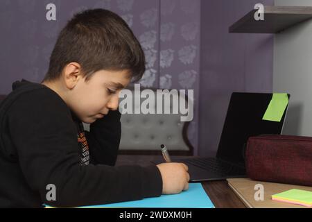 Online-Fernunterricht. Schuljunge studiert zu Hause und macht Hausaufgaben. Gelangweilter Student, der versucht, Komposition zu schreiben. Bleiben Sie zu Hause. Stockfoto