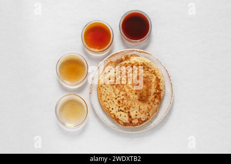 Verschiedene Klassen von Ahornsirupe in verschiedenen Farben in Glasschalen mit Pfannkuchen daneben Stockfoto