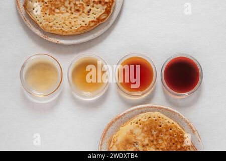 Verschiedene Klassen von Ahornsirupe in verschiedenen Farben in Glasschalen mit Pfannkuchen daneben Stockfoto