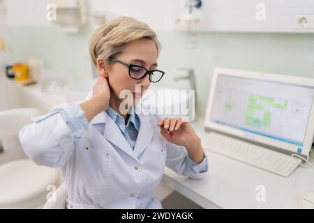 Porträt einer müden Ärztin mittleren Alters in Brille mit Nackenschmerzen während der Arbeit am Laptop, die im Krankenhaus verletzt wurde. Stockfoto