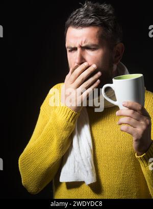 Kranker Mann im Pullover, in Schal mit einer Tasse Medizintee gewickelt. Gutaussehender Kerl mit Halsschmerzen. Bärtiger Mann mit Grippe und Fieber, der Heilung trinkt Stockfoto