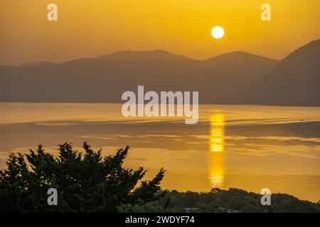 Sonnenaufgang hinter den Bergen des griechischen Festlandes von der Insel Meganisi im Ionischen Meer Stockfoto