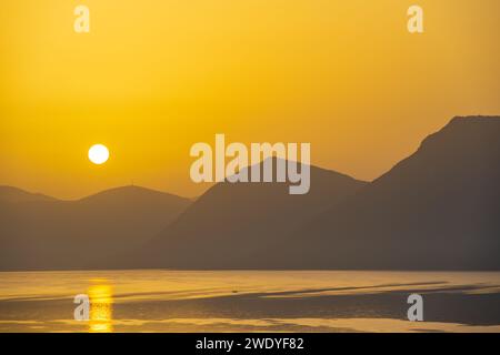 Sonnenaufgang hinter den Bergen des griechischen Festlandes von der Insel Meganisi im Ionischen Meer Stockfoto