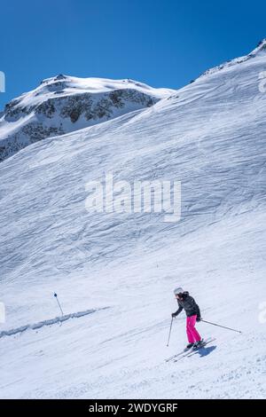 Ein Skifahrer in leuchtend rosa Hosen zieht anmutig einen malerischen, schneebedeckten Berghang hinab Stockfoto