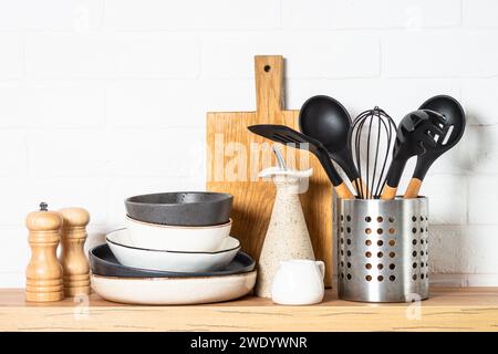 Küchentisch, Küchenutensilien, Teller, Schüsseln, Schüttler und Holzschneidebrett. Stockfoto
