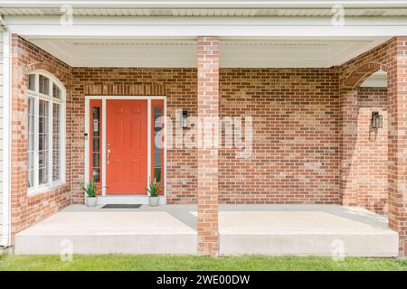 Die rote Haustür eines Hauses ist von roten Ziegeln und Pflanzen umgeben, die vor den Fenstern sitzen. Stockfoto