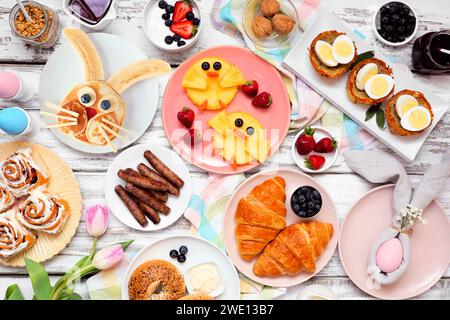 Osterfrühstück oder Brunch-Tisch. Draufsicht auf weißem Holzhintergrund. Hasenpfannkuchen, Eiernester, Hühnerfrüchte und eine Sammlung von Frühlingsnahrungsmitteln Stockfoto