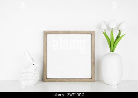 Holzrahmen mit Osterdekor auf weißem Regal. Häschen und Tulpenblumen stricken. Quadratischer Rahmen an einer weißen Wand. Kopierbereich. Stockfoto