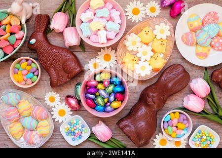 Osterbonbons. Tischszene mit Draufsicht über einem Holzhintergrund. Schokoladenhasen, Süßigkeiten und eine Auswahl an Süßigkeiten. Stockfoto