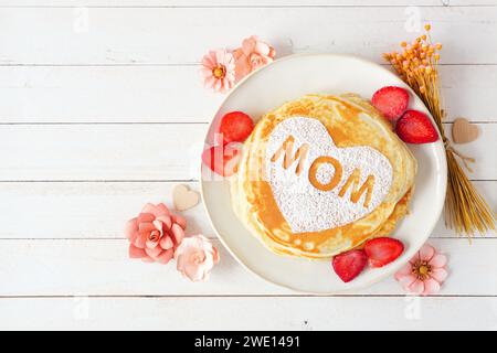 Pfannkuchen mit Herzform und MAMA-Buchstaben. Frühstückskonzept zum Muttertag. Blick von oben vor weißem Holzhintergrund. Stockfoto