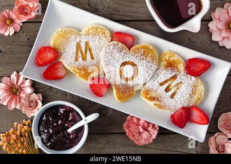 Herzförmige Pfannkuchen mit MUTTI-Buchstaben. Frühstückskonzept zum Muttertag. Über dem Tisch auf rustikalem Holzhintergrund. Stockfoto