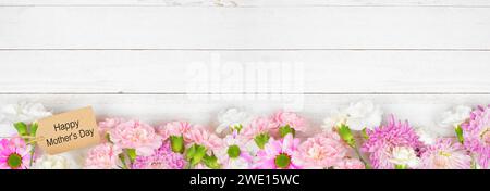 Happy Mothers Day Geschenkanhänger mit langem unteren Rand aus rosa und weißen Blumen. Draufsicht auf weißem Holzbanner Hintergrund. Kopierbereich. Stockfoto