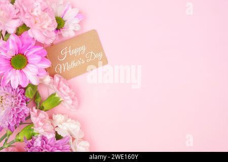 Geschenk-Anhänger zum Happy Mothers Day mit seitlichem Rand aus rosa und weißen Blumen. Draufsicht auf rosafarbenem Hintergrund. Kopierbereich. Stockfoto