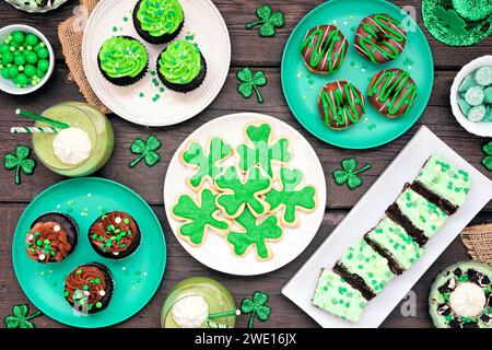 Desserts zum St. Patricks Day. Tischszene auf dunklem Holzhintergrund. Shamrock-Kekse, grüne Cupcakes, Brownies, Donuts und Süßigkeiten. Ansicht oben. Stockfoto