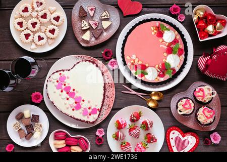 Valentinstag-Tischszene mit einer Auswahl an Desserts und Süßigkeiten. Ansicht von oben nach unten auf dunklem Holzhintergrund. Das Thema Liebe und Herzen. Stockfoto