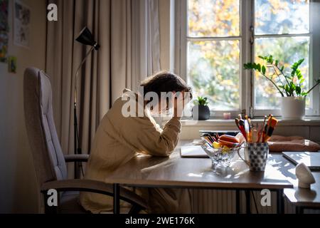 Müde erschöpfte Frau, die am Tisch sitzt und am frühen Morgen nach der Arbeit den Kopf hielt. Stockfoto