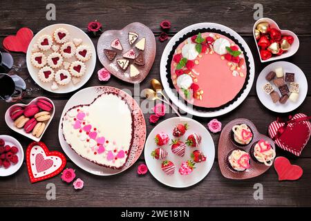 Valentinstag-Tischszene mit einer Auswahl an Desserts und Süßigkeiten. Blick von oben auf dunklem Holzhintergrund. Das Thema Liebe und Herzen. Stockfoto