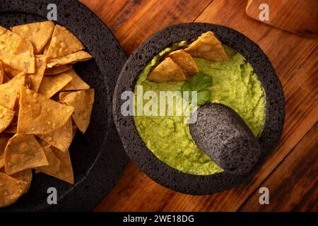 Guacamol. Avocado-Dip mit Tortilla-Chips, auch Nachos genannt, serviert in einer Schüssel aus vulkanischem Steinmörtel und Pistill, bekannt als Molcajete. Mexikanisch Stockfoto