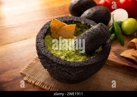 Guacamol. Avocado-Dip mit Tortilla-Chips, auch Nachos genannt, serviert in einer Schüssel aus vulkanischem Steinmörtel und Pistill, bekannt als Molcajete. Mexikanisch Stockfoto