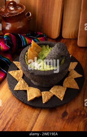 Guacamol. Avocado-Dip mit Tortilla-Chips, auch Nachos genannt, serviert in einer Schüssel aus vulkanischem Steinmörtel und Pistill, bekannt als Molcajete. Mexikanisch Stockfoto