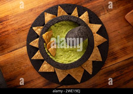 Guacamol. Avocado-Dip mit Tortilla-Chips, auch Nachos genannt, serviert in einer Schüssel aus vulkanischem Steinmörtel und Pistill, bekannt als Molcajete. Mexikanisch Stockfoto