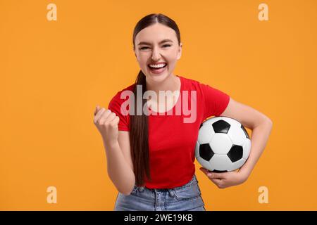 Glücklicher Fußballfan mit Ball, der auf orangefarbenem Hintergrund feiert Stockfoto