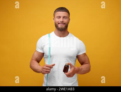 Sportlicher junger Mann mit Maßband und Flasche Supplemente auf orangem Hintergrund. Gewichtsverlust Stockfoto