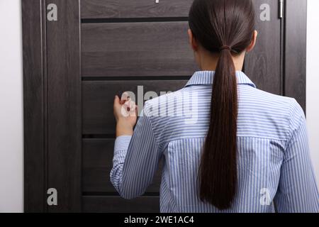 Frau klopft drinnen an die Tür, Rückansicht. Leerzeichen für Text Stockfoto