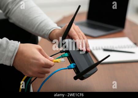 Mann, der Kabel in den WLAN-Router an einem Holztisch drinnen steckt, Nahaufnahme Stockfoto