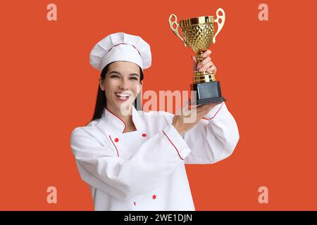 Weibliche Köchin mit goldener Tasse auf orangefarbenem Hintergrund Stockfoto